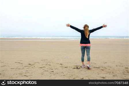 Back view of young woman watching the sea in autumn with hands up. Young woman watching the sea with hands up