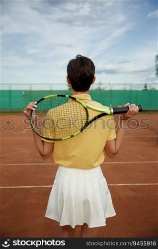 Back view on young teenage woman tennis player holding racket on shoulders. Recreational activity and professional sport concept. Back view on young teenage woman tennis player holding racket