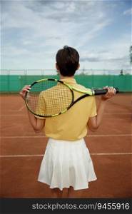 Back view on young teenage woman tennis player holding racket on shoulders. Recreational activity and professional sport concept. Back view on young teenage woman tennis player holding racket