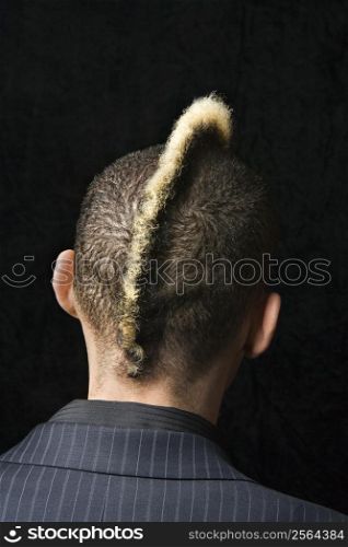 Back view portrait of Caucasian man in suit with mohawk against black background.