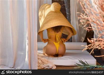 Back view young woman in bikini and straw hat sitting and relaxing in lounge area of spa hotel resort. Back view young woman in bikini and straw hat