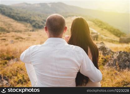 Back viw of young couple man and woman girl hugging embracing in nature on mountain range in autumn day evening field