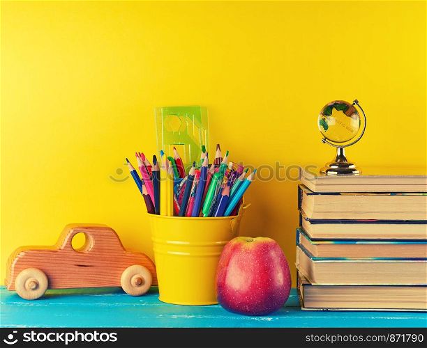 background back to school with children's stationery pencils, books, apple, glass globe on a blue background