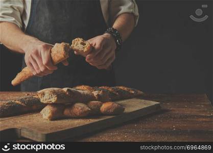 Background blur. On the background of an old brown wooden table Baker man holds halves of baguettes in his hands.pshape on a wooden board.. The baker keeps the baguette halves in his hands.