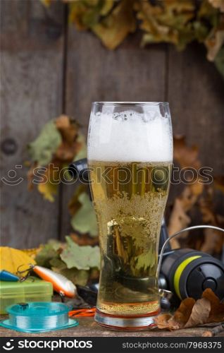 background for oktoberfest with fishing tackles and glass a beer on old wooden board with oak leaf
