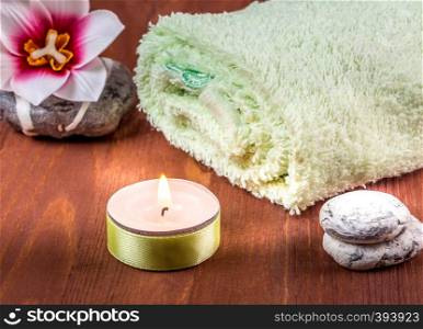 Background for spa. Towel, candle and stones. Rolled towel, burning candle and stones on wooden background
