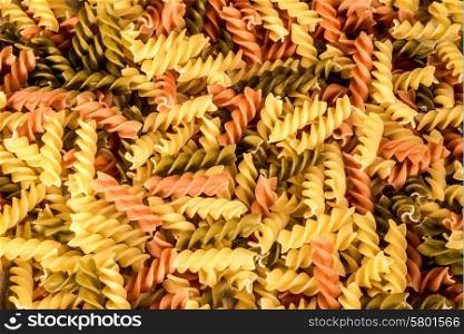 Background image of three different colours of fussili pasta.