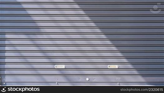 Background of automatic gray metal roller shutter door with sunlight and shadow on surface