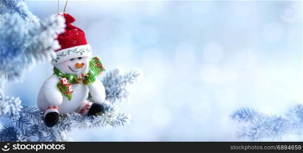 Background of Christmas Snowman in Santa Hat Hanging on a Tree Branch in the Snow Winter Forest, Copy Space