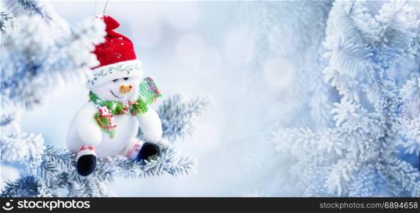 Background of Christmas Snowman in the Red Santa Hat Hanging on a Tree Branch in the Snow Winter Forest, Copy Space