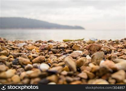 Background of colorful beach pebbles of different shape and size with view of sea and sky on background.Selective focus.. Background of colorful beach pebbles of different shape and size