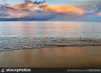 Background of gentle waves on golden sand beach with ocean and colorful sunset sky behind