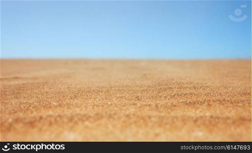 Background with dry beach sand and clear blue sky close-up
