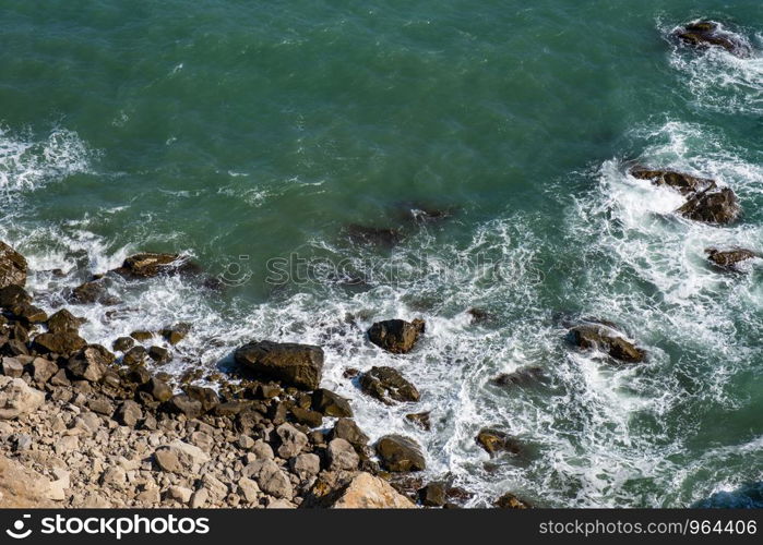 Background with rocky seashore and white surf foam on a summer sunny day.