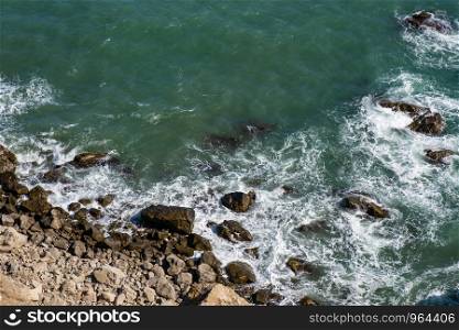 Background with rocky seashore and white surf foam on a summer sunny day.