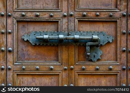 Backgrounds and textures: ancient wooden door, closed with traditional forged metal lock. Ancient door with forged metal lock