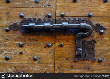 Backgrounds and textures: ancient wooden door, closed with traditional forged metal lock. Ancient door with forged metal lock