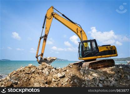 backhoe loader digger excavator stone working construction site on the beach sea ocean and blue sky background