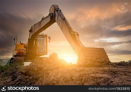 Backhoe parked at construction site after digging soil. Bulldozer on sunset sky and clouds background. Digger after work. Earth moving machine at construction site at dusk. Digger with dirt bucket.