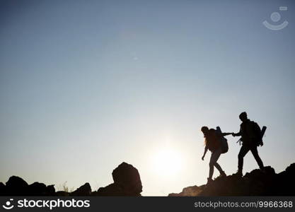 Backlit dark silhouettes of couple hiking in mountains, young man following girlfriends holding hands, side view graphic image