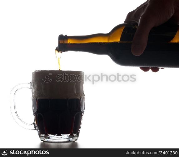Backlit isolated beer tankard with dark ale being poured from brown bottle and creating a large head of froth on the liquid