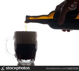Backlit isolated beer tankard with dark ale being poured from brown bottle and creating a large head of froth on the liquid