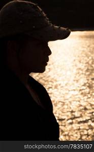 Backlit silhouette of a woman wearing a hat. Sop freckled sunlight reflecting off the surface of the sea in the evening.