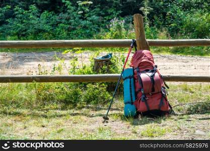 Backpack and trekking pole standing near fence at green grass countryside. Travel outdoor background