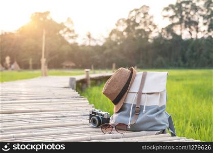 Backpack with hat and camera on bamboo path at green paddy field, Travel concept