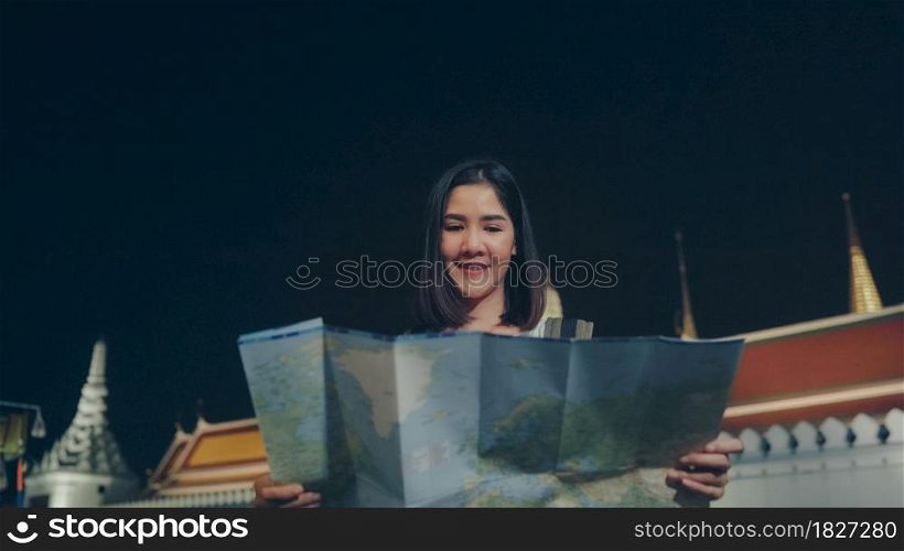 Backpacker Asian woman travel in Bangkok, Thailand. Young Asian tourist girl looking maps for direction places at night while walk along the street enjoying the journey holiday travel concept.