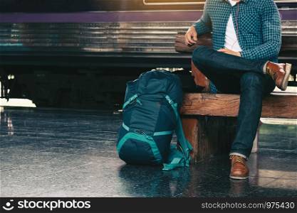 Backpacker man sitting on bench waiting at train station.