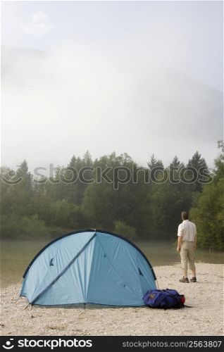 Backpacker standing beside his tent in a mountain landscape in the morning