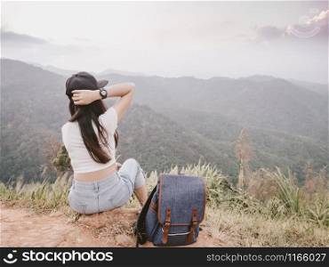 backside of hipster girl with backpack, enjoying sit see to valley landscape view on peak mountains in tropical rainforest. solo traveling concept.