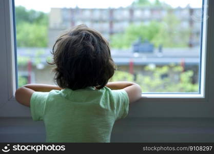 Backview of a lonely little boy looking out of the window