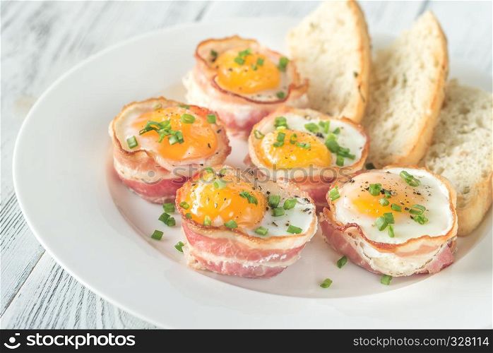 Bacon and egg cups with slices of toasted bread on the white plate