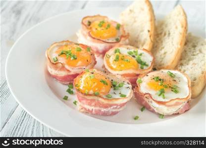 Bacon and egg cups with slices of toasted bread on the white plate