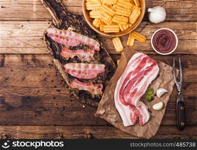 Bacon flavored snacks chips with grilled bacon rashers on vintage chopping board with smoked raw bacon on butchers paper garlic and sauce on wood background.