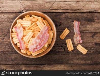 Bacon flavoured snacks chips in wooden bowl with grilled bacon rashers on wood background.