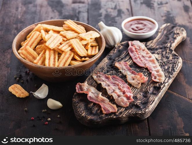 Bacon flavoured snacks with grilled bacon rashers on vintage chopping board with garlic and sauce on wood background.
