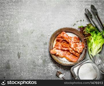 Bacon in a frying pan with salt and herbs. On a stone background.. Bacon in a frying pan with salt and herbs.