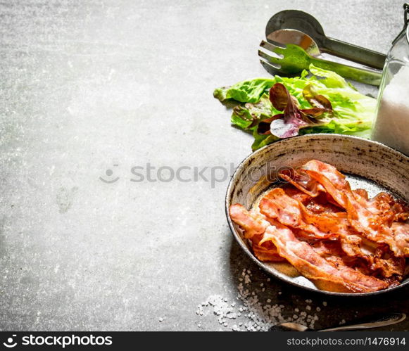 Bacon in a frying pan with salt and herbs. On a stone background.. Bacon in a frying pan with salt and herbs.