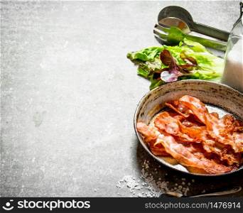 Bacon in a frying pan with salt and herbs. On a stone background.. Bacon in a frying pan with salt and herbs.