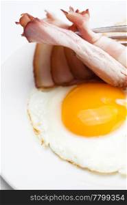 bacon with fried eggs on a plate, fork and bread isolated on white