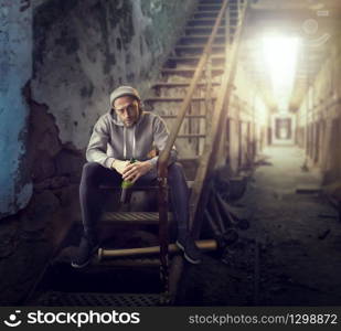 Bad guy with bottle of alcohol sits on stairs. Street robber waiting for victim. Crime concept