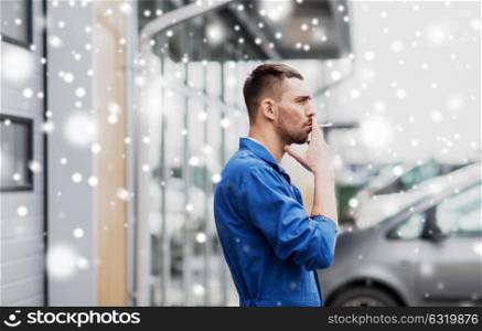 bad habits and people concept - auto mechanic smoking cigarette at car shop or garage outdoors over snow. auto mechanic smoking cigarette at car workshop