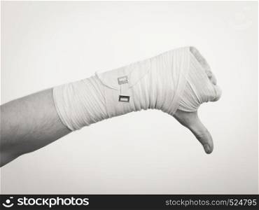 Bad news and information. Medicine aspects. Male hand with bandage showing thumb down sign symbol.. Male bandaged hand with thumb down sign.