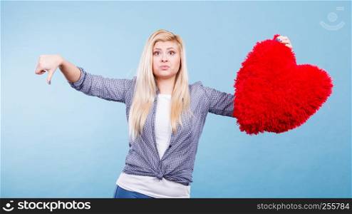 Bad relationship, independence concept. Woman holding big red fluffy pillow in heart shape showing thumb down gesture.. Woman holding red heart showing thumb down