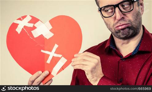 Bad relationships, breaking up, sadness emotions concept. Sad adult man holding broken heart, on grey. Sad adult man holding broken heart