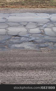 Bad road with cracks and the part of the ground and grass