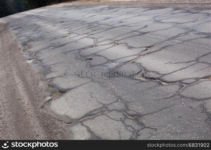 Bad road with cracks and the part of the ground and grass
